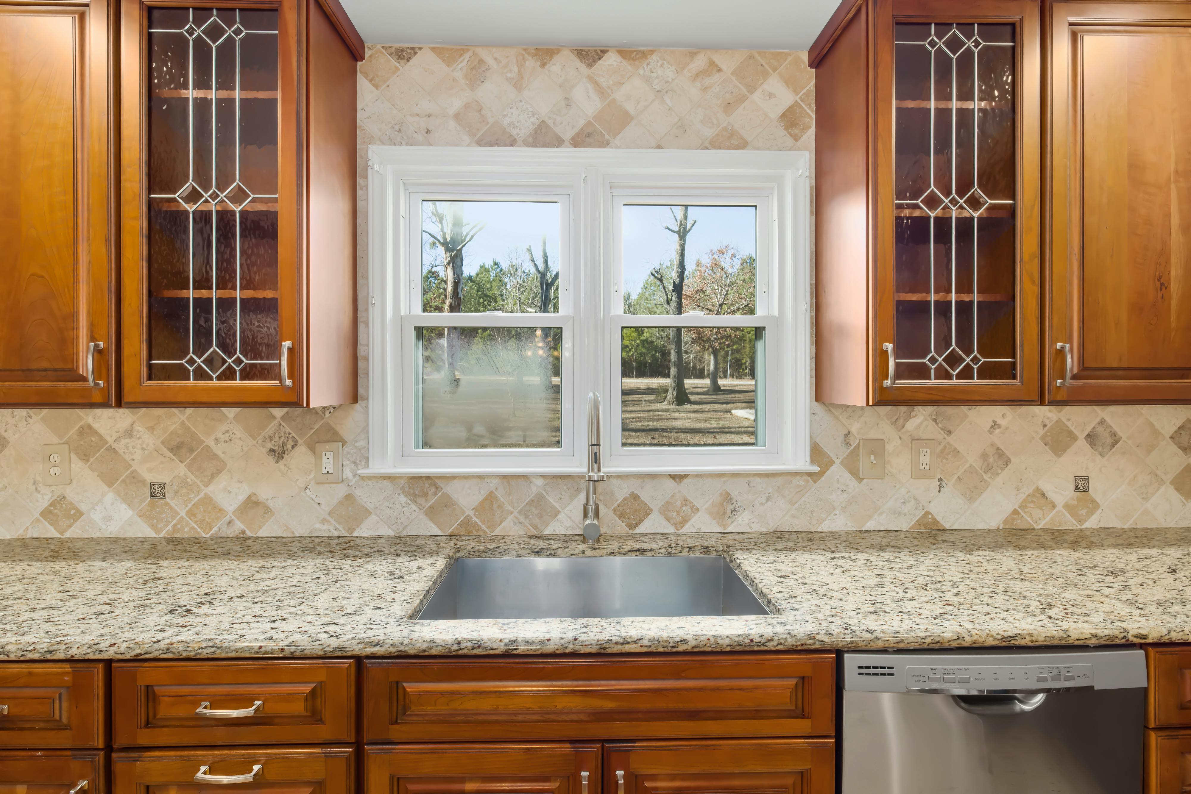 Modern kitchen with stainless steel sink, granite countertop, wooden cabinets, and tiled backsplash, perfect for showcasing durable and stylish kitchen sink materials.